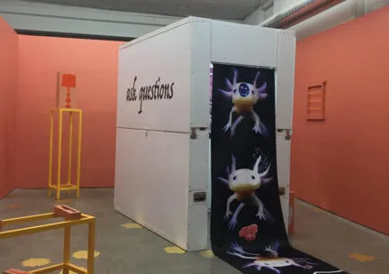 Installation of a portable, phone booth-sized art gallery, inside of a bigger art gallery with salmon colored walls.